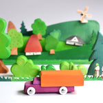 Bumbu wooden waldorf lorry toy on a white table in front of a green wooden toy landscape scene