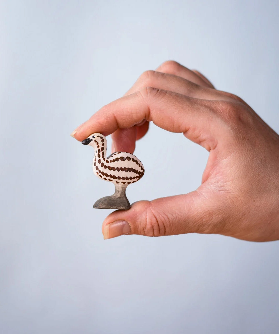 A hand holding the Bumbu wooden emu chick figure