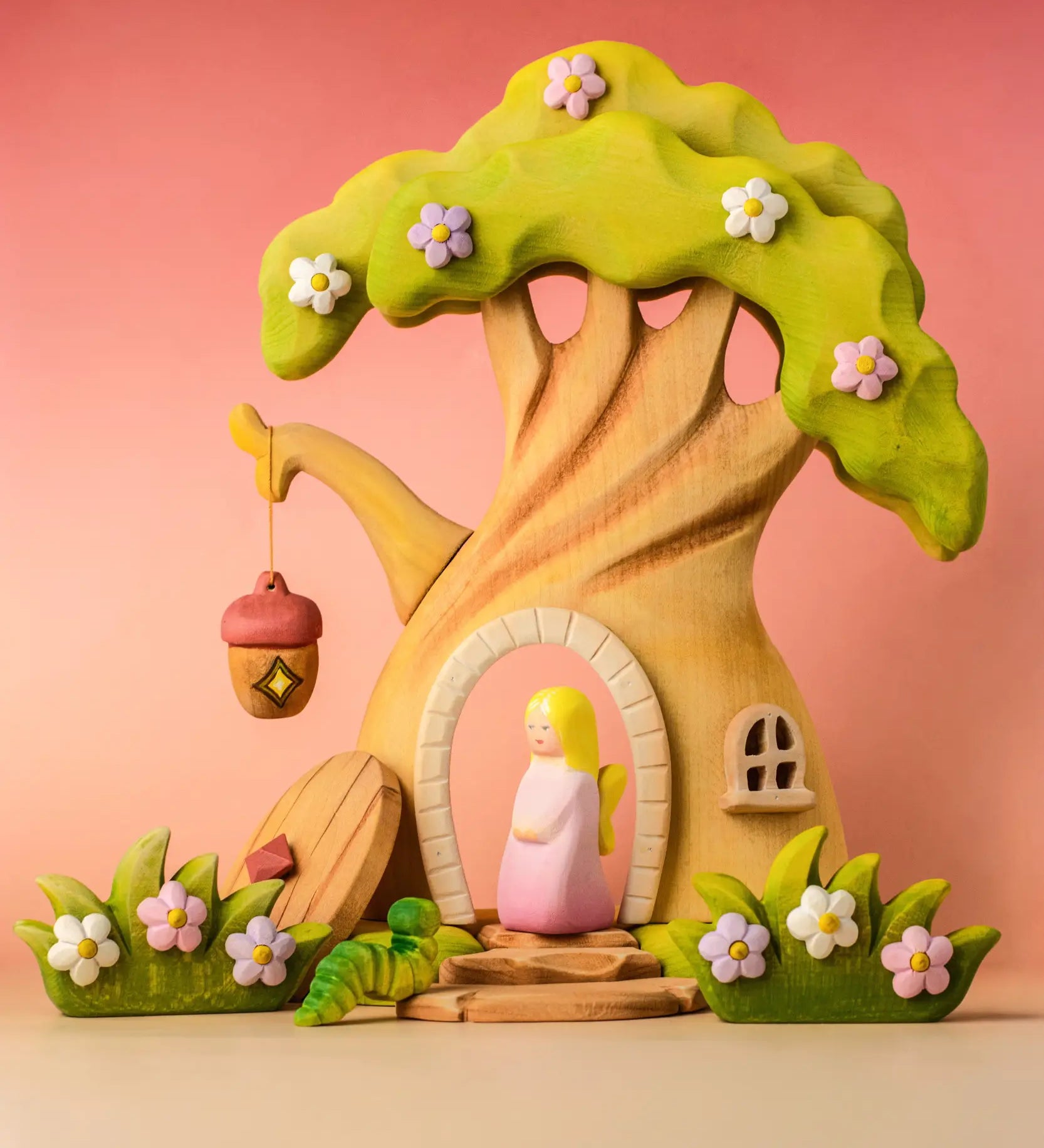 Bumbu wooden fairy treehouse with a pink fairy figure standing in the doorway with wooden blossom bushes either side