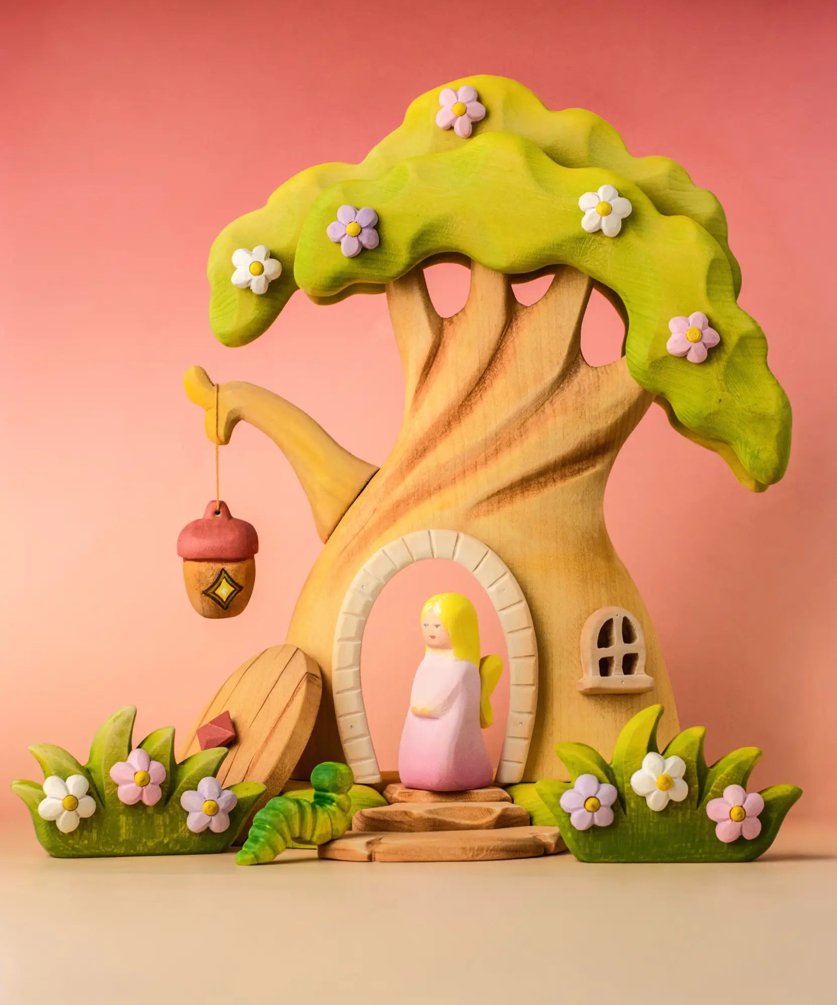 Bumbu wooden fairy treehouse with a pink fairy figure standing in the doorway with wooden blossom bushes either side