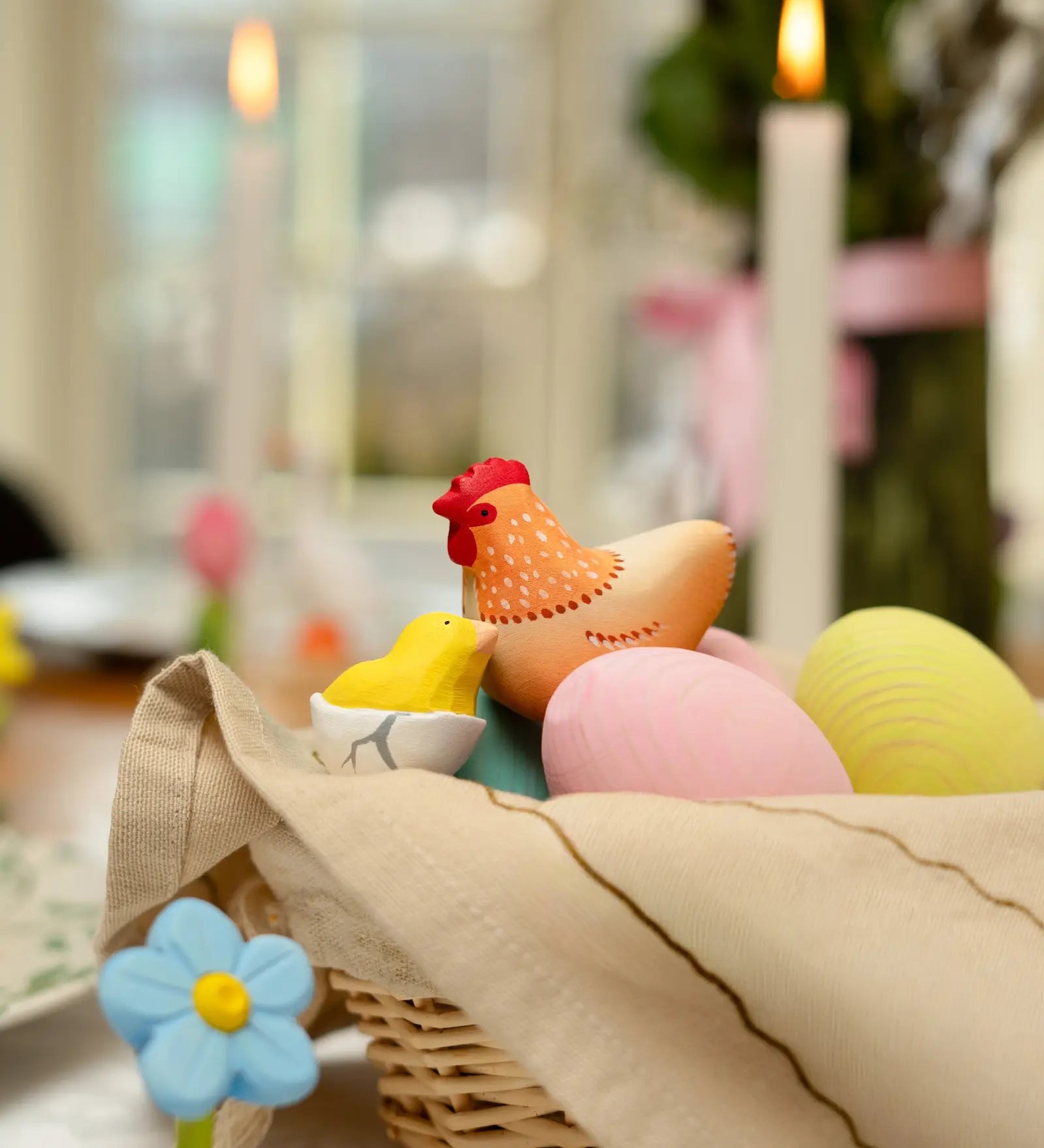 Handcrafted wooden Bumbu hen figure next to a yellow chick and eggs in a wicker basket.