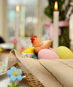 Handcrafted wooden Bumbu hen figure next to a yellow chick and eggs in a wicker basket.
