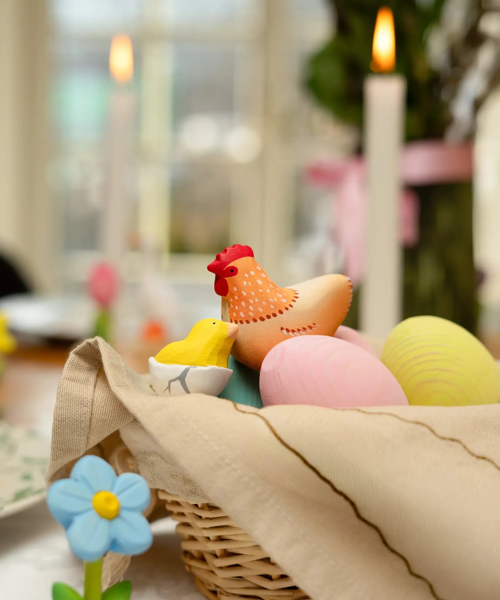 Handcrafted wooden Bumbu hen figure next to a yellow chick and eggs in a wicker basket.