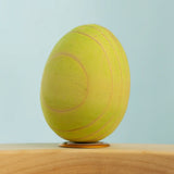 Bumbu wooden hand painted festive green egg decorative figure standing in a celebration ring with a blue background