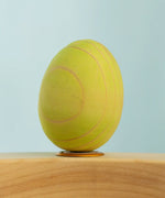 Bumbu wooden hand painted festive green egg decorative figure standing in a celebration ring with a blue background