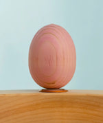 Bumbu wooden hand painted festive pink egg decorative figure standing in a celebration ring with a blue background