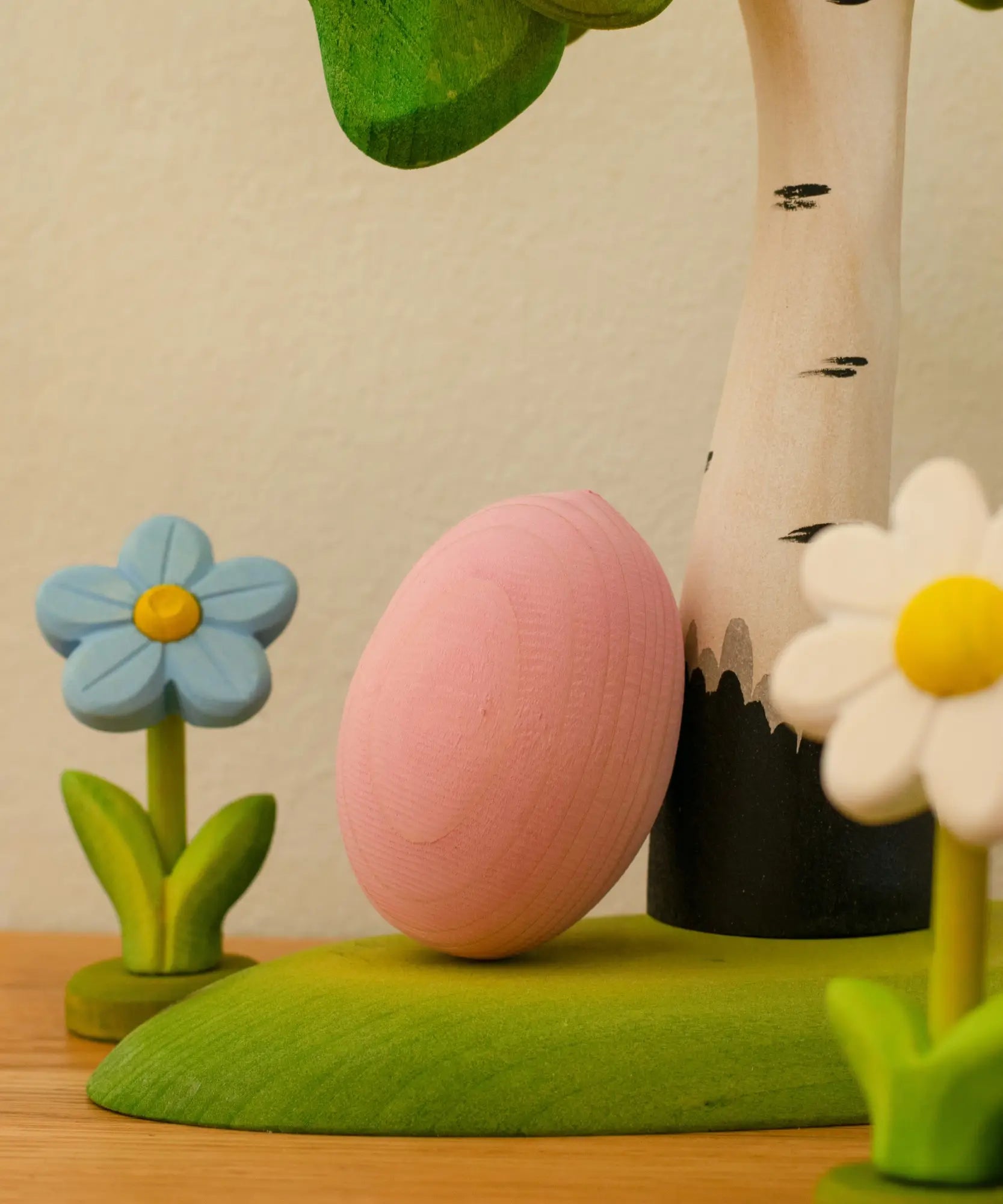 Bumbu handcrafted wooden egg decorative figure in pink resting on a tree with spring flowers