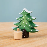 Bumbu Festive Tree Celebration decorative Figure to fit on a Grimm's celebration ring. The figure is a green fir tree decorated with snow. The wooden tree is shown separated from the wooden base it comes with.  These festive figures are perfect for your Christmas celebration ring set up. These expertly hand crafted items are part of a large range of wooden toys available here at Babipur. 