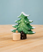 Bumbu Festive Tree Celebration decorative Figure to fit on a Grimm's celebration ring. The figure is a green fir tree decorated with snow. The wooden tree is shown separated from the wooden base it comes with.  These festive figures are perfect for your Christmas celebration ring set up. These expertly hand crafted items are part of a large range of wooden toys available here at Babipur. 
