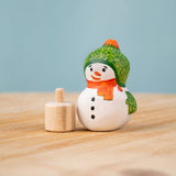 Bumbu Festive Snowman Celebration decorative Figure to fit on a Grimm's celebration ring. The hand painted snowman figure has a green hat with matching gloves and an orange scarf. The figure is shown separated from the wooden base that it comes with. These festive figures are perfect for your Christmas celebration ring set up. These expertly hand crafted items are part of a large range of wooden toys available here at Babipur. 