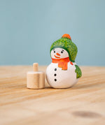 Bumbu Festive Snowman Celebration decorative Figure to fit on a Grimm's celebration ring. The hand painted snowman figure has a green hat with matching gloves and an orange scarf. The figure is shown separated from the wooden base that it comes with. These festive figures are perfect for your Christmas celebration ring set up. These expertly hand crafted items are part of a large range of wooden toys available here at Babipur. 