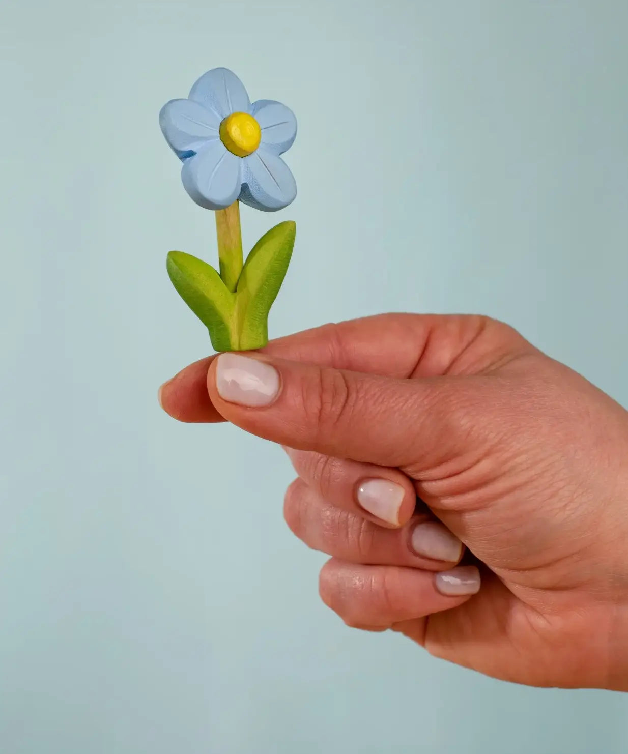 Adult hand holding the Bumbu handcrafted wooden blue forget me not decorative figure showing size