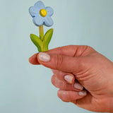 Adult hand holding the Bumbu handcrafted wooden blue forget me not decorative figure showing size
