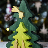 A Bumbu Christmas Tree Nativity Puzzle in the Gold colour way placed in front of a Christmas tree. 