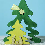 A Bumbu Christmas Tree Nativity Puzzle in the Gold colour way placed on a wooden surface. The light green tree piece has been pulled forward. 
