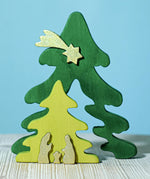 A Bumbu Christmas Tree Nativity Puzzle in the Gold colour way placed on a wooden surface. The light green tree piece has been pulled forward. 