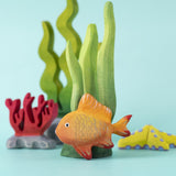 The Bumbu hand made wooden goldfish toy figure, in an ocean playscene with seaweed and coral.