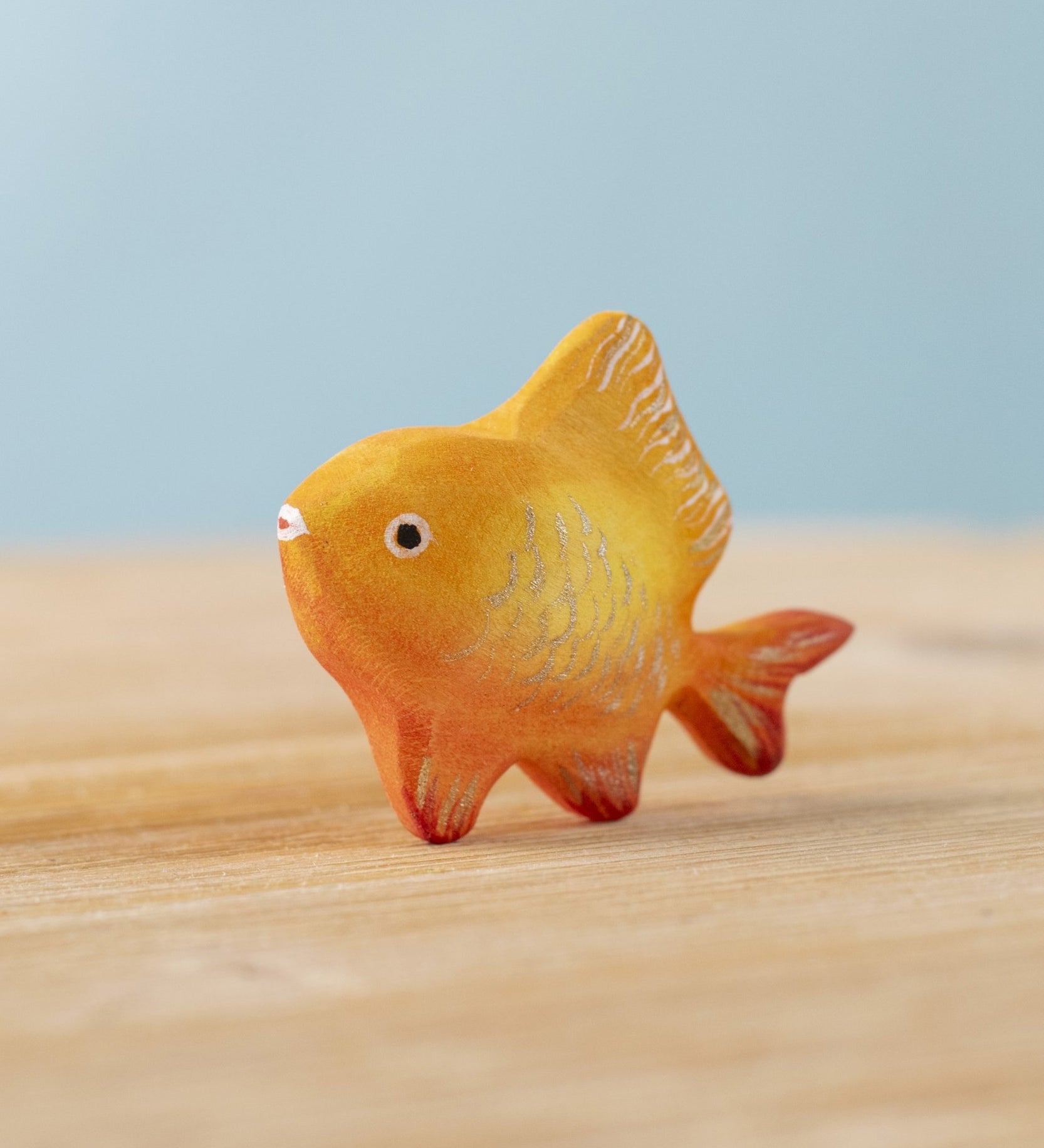 The Bumbu hand carved wooden toy goldfish figure from Bumbu, painted in orange with sparkly golden scales.