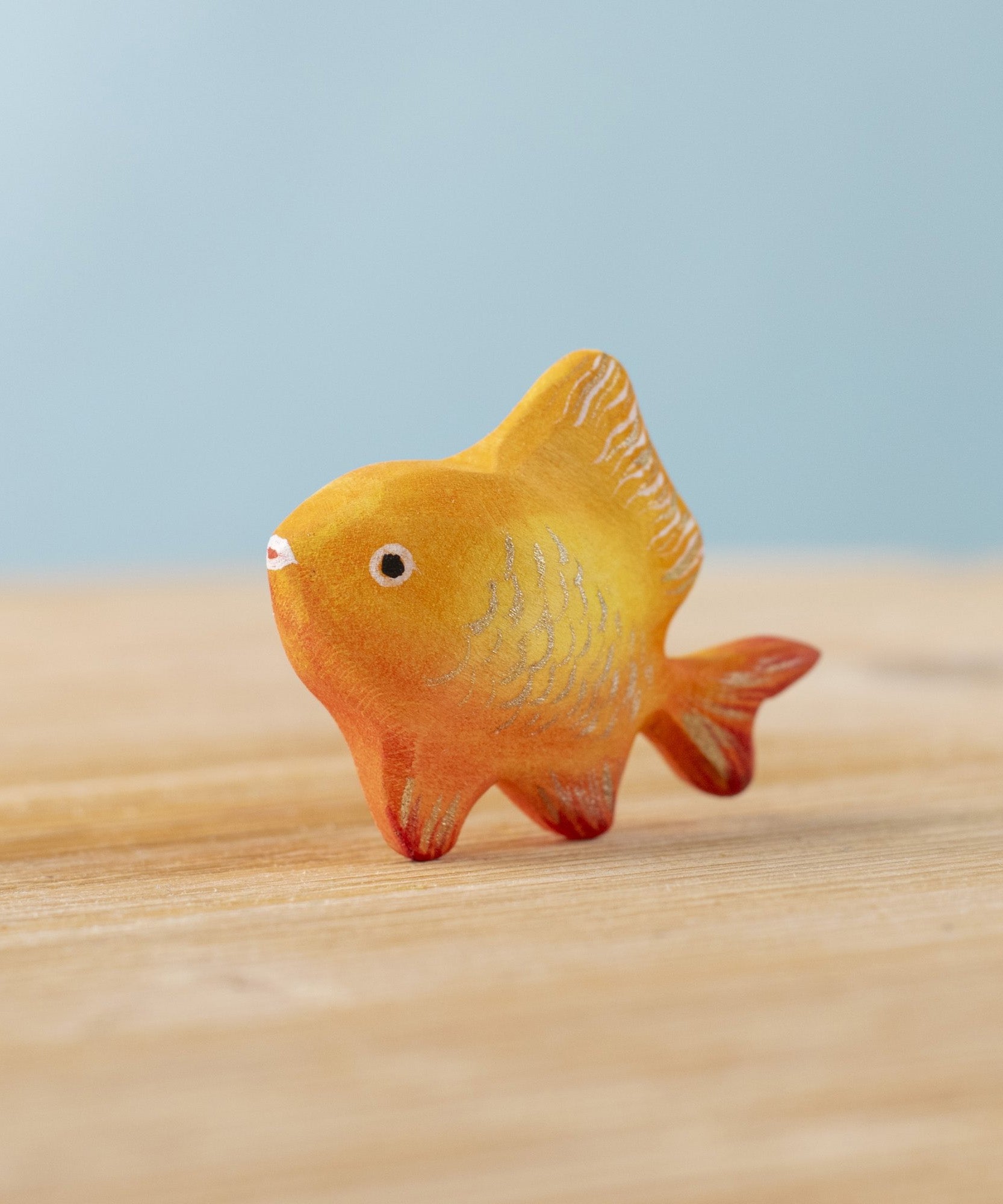 The Bumbu hand carved wooden toy goldfish figure from Bumbu, painted in orange with sparkly golden scales.