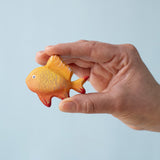 A hand holding the Bumbu wooden goldfish toy for size reference.