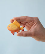 A hand holding the Bumbu wooden goldfish toy for size reference.