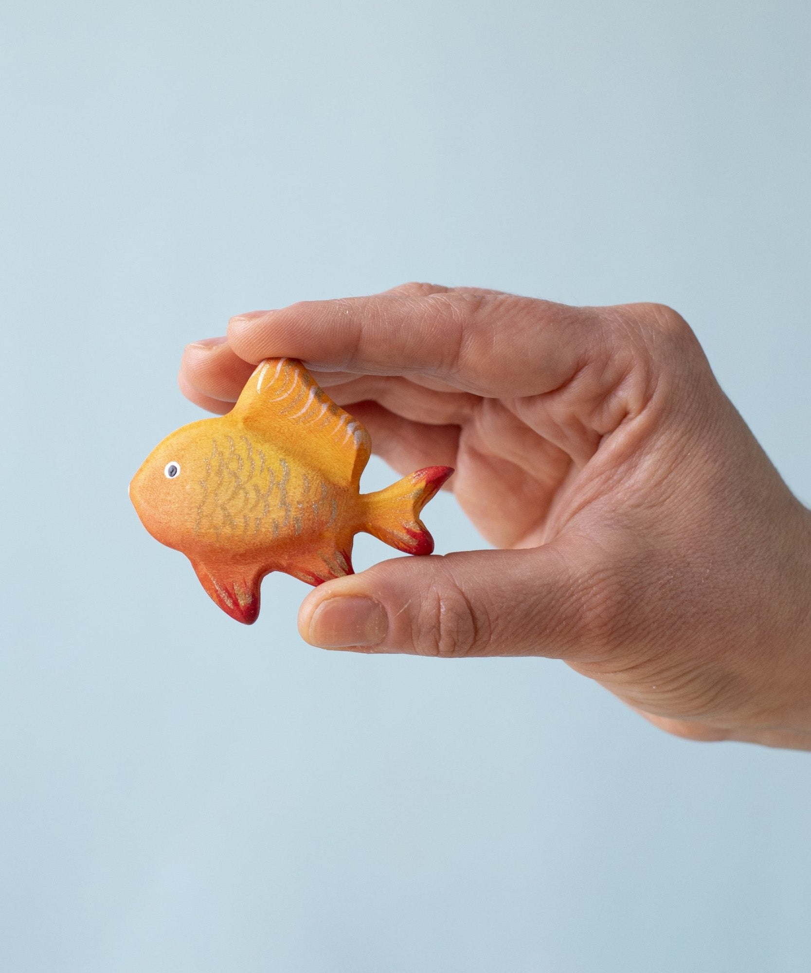 A hand holding the Bumbu wooden goldfish toy for size reference.