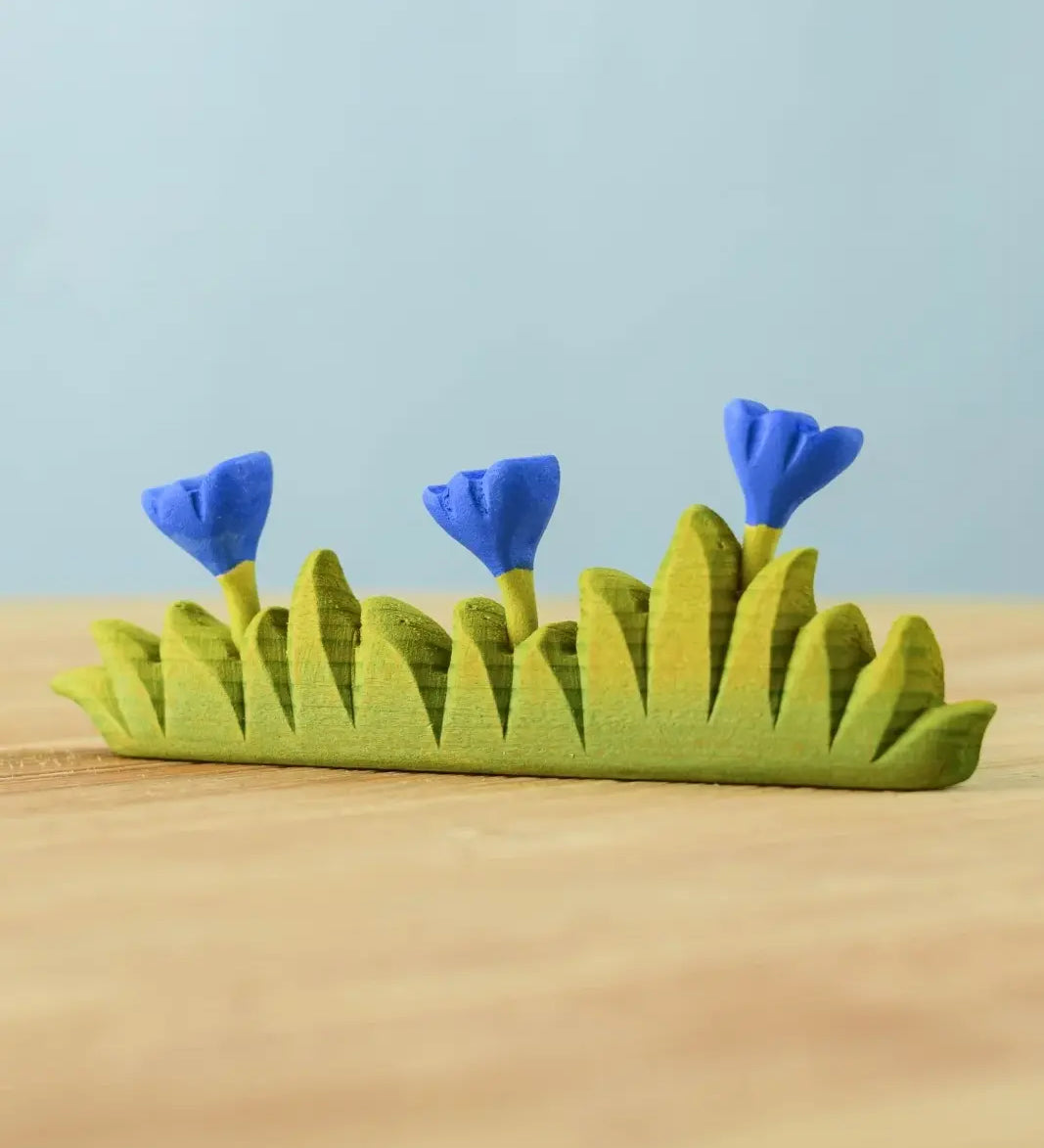 Bumbu large grass with 3 blue flowers wooden toy scenery piece placed on a wooden surface. 