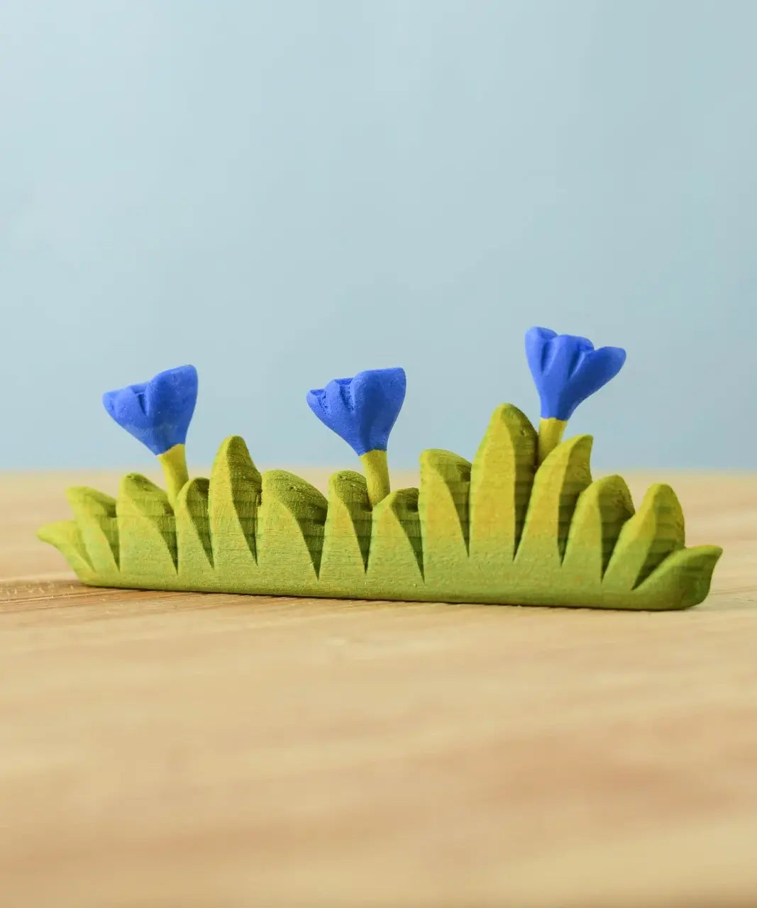 Bumbu large grass with 3 blue flowers wooden toy scenery piece placed on a wooden surface. 