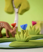 Bumbu small wooden grass with blue flower placed at the front of small world play scene with deer and trees in the background.