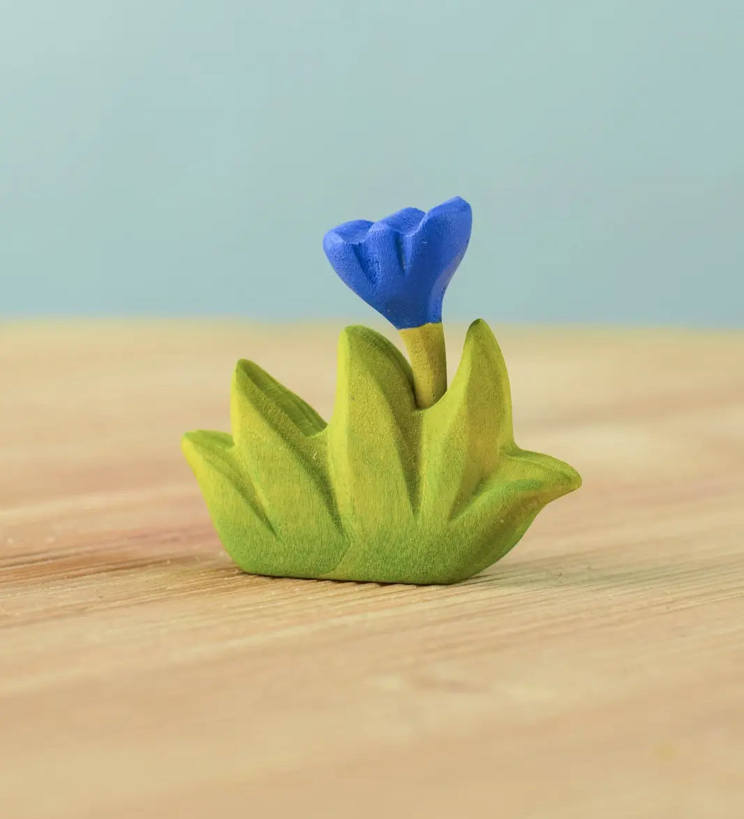 Bumbu small wooden grass with blue flower for use as scenery in small world play placed on a wooden surface.