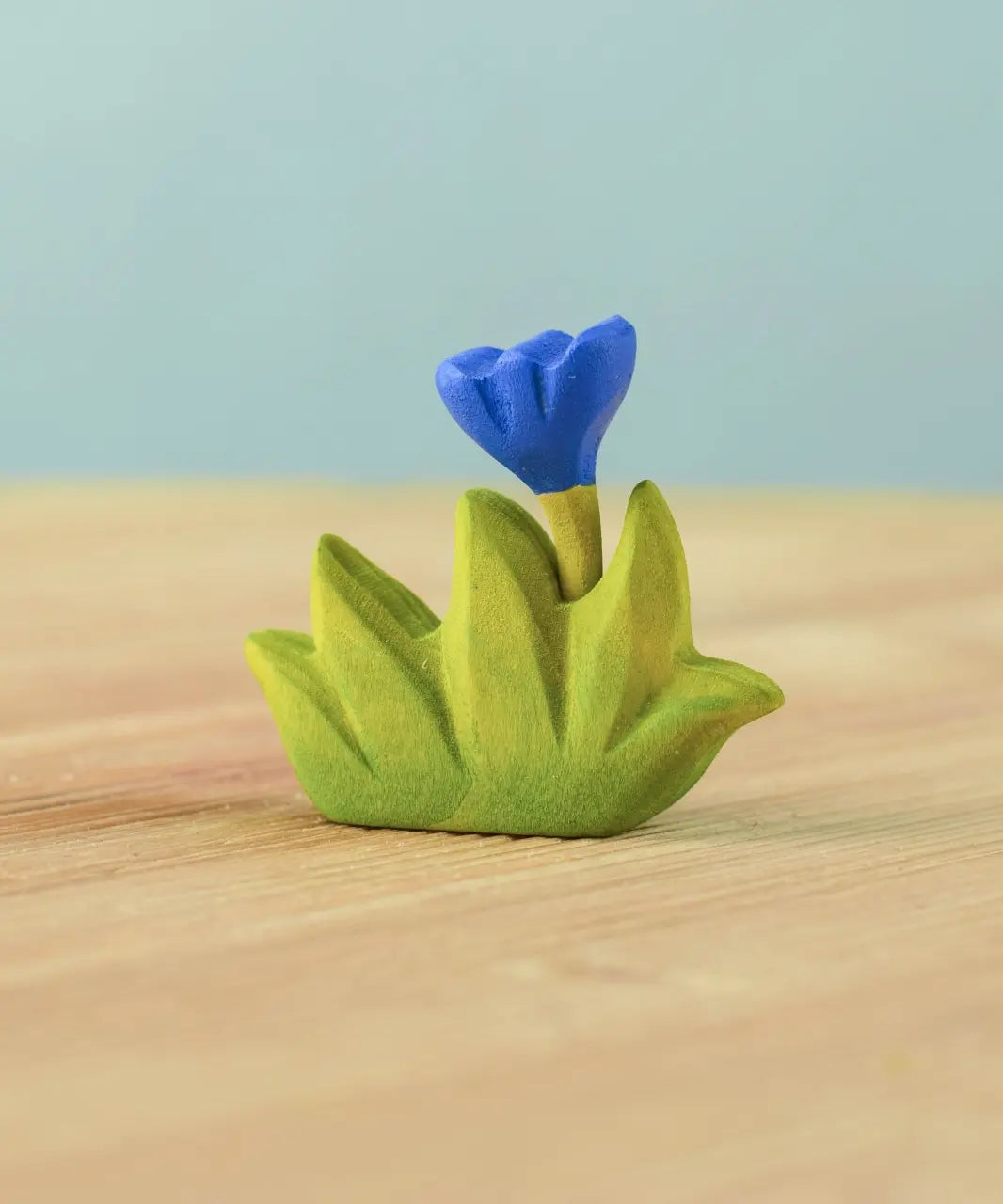 Bumbu small wooden grass with blue flower for use as scenery in small world play placed on a wooden surface.