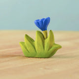 Bumbu small wooden grass with blue flower for use as scenery in small world play placed on a wooden surface.
