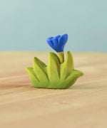 Bumbu small wooden grass with blue flower for use as scenery in small world play placed on a wooden surface.