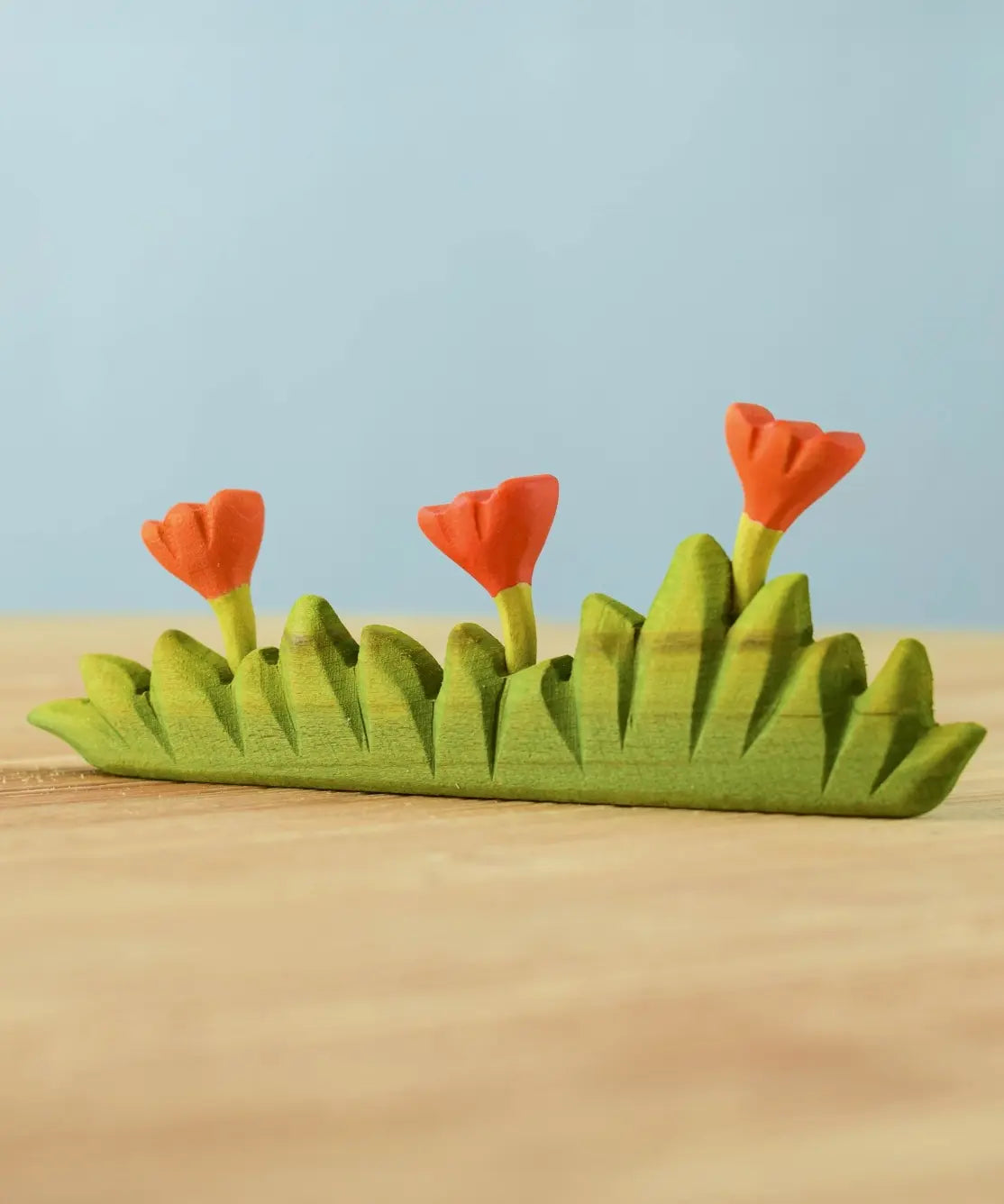 Bumbu large grass with three orange flowers wooden toy scenery placed on a wooden surface.