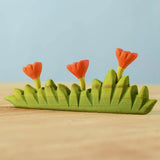 Bumbu large grass with three orange flowers wooden toy scenery placed on a wooden surface.