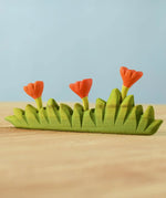 Bumbu large grass with three orange flowers wooden toy scenery placed on a wooden surface.