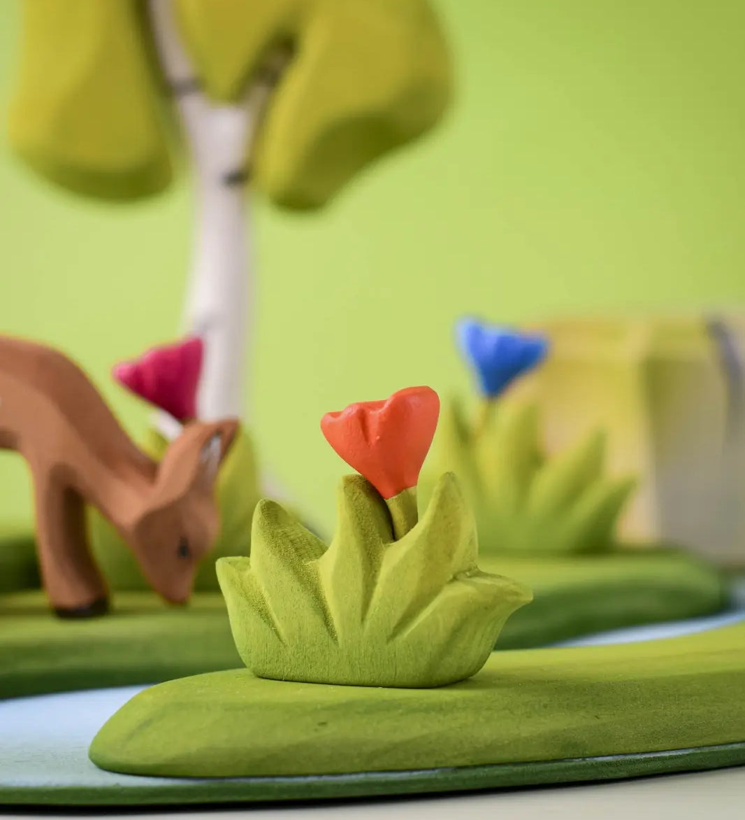 Bumbu small wooden grass with orange flower scenery piece placed in a small world play scene with deer, flowers and trees in the background.