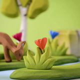 Bumbu small wooden grass with orange flower scenery piece placed in a small world play scene with deer, flowers and trees in the background.