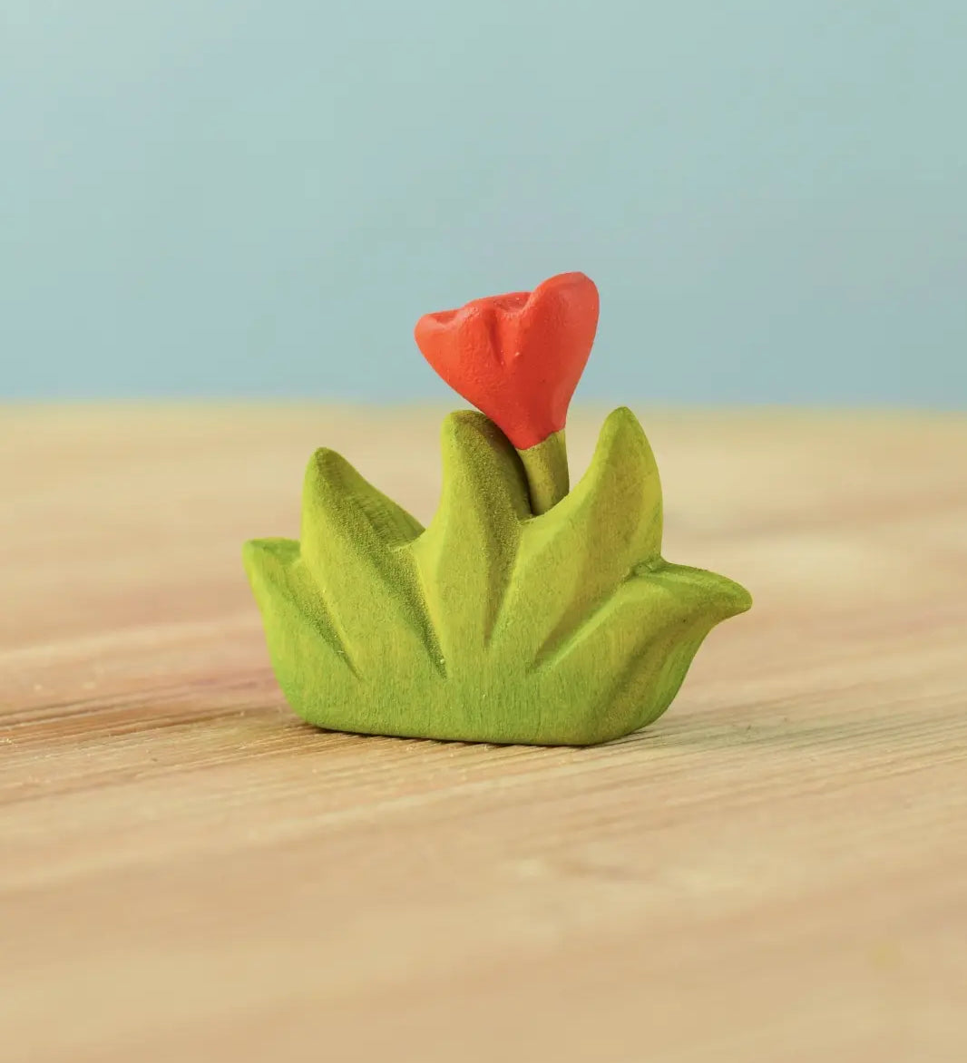Bumbu small wooden grass with orange flower scenery piece placed on a wooden surface.