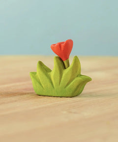 Bumbu small wooden grass with orange flower scenery piece placed on a wooden surface.