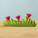Bumbu large wooden grass with three pink flowers toy scenery piece placed on a wooden surface. 