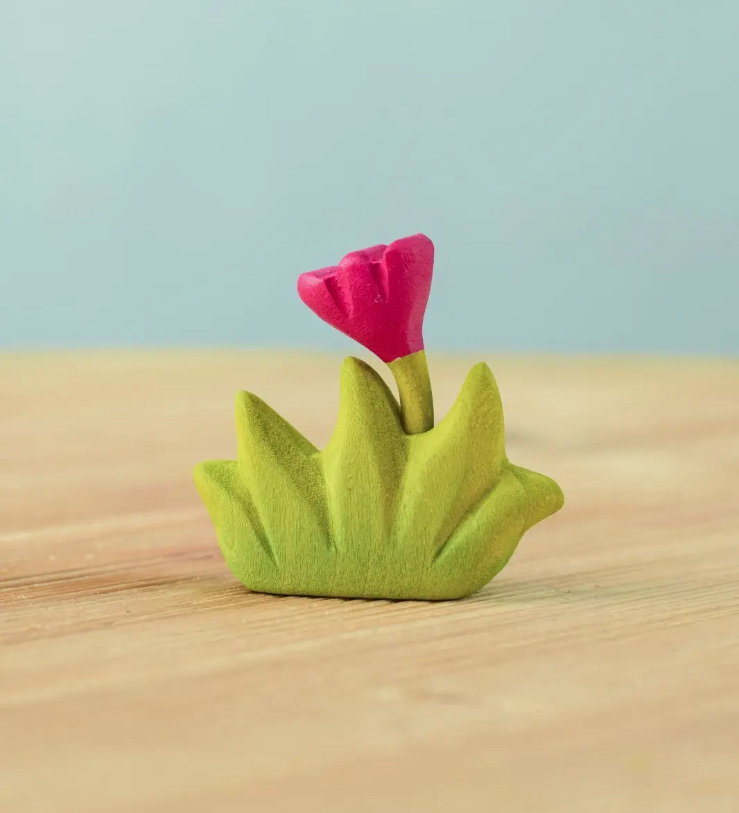 Bumbu small wooden grass with pink flower for use as scenery in small world play placed on a wooden surface.
