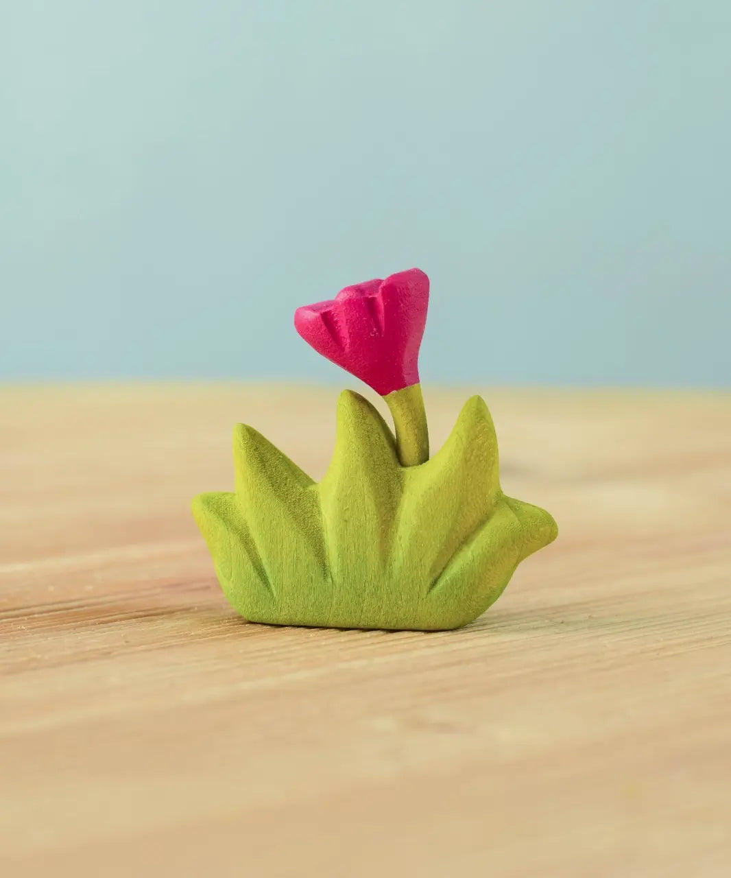 Bumbu small wooden grass with pink flower for use as scenery in small world play placed on a wooden surface.