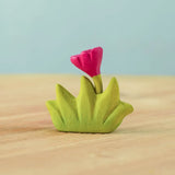 Bumbu small wooden grass with pink flower for use as scenery in small world play placed on a wooden surface.
