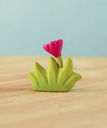 Bumbu small wooden grass with pink flower for use as scenery in small world play placed on a wooden surface.