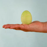 Adult hand holding the Bumbu handcrafted festive green egg decorative figure showing size