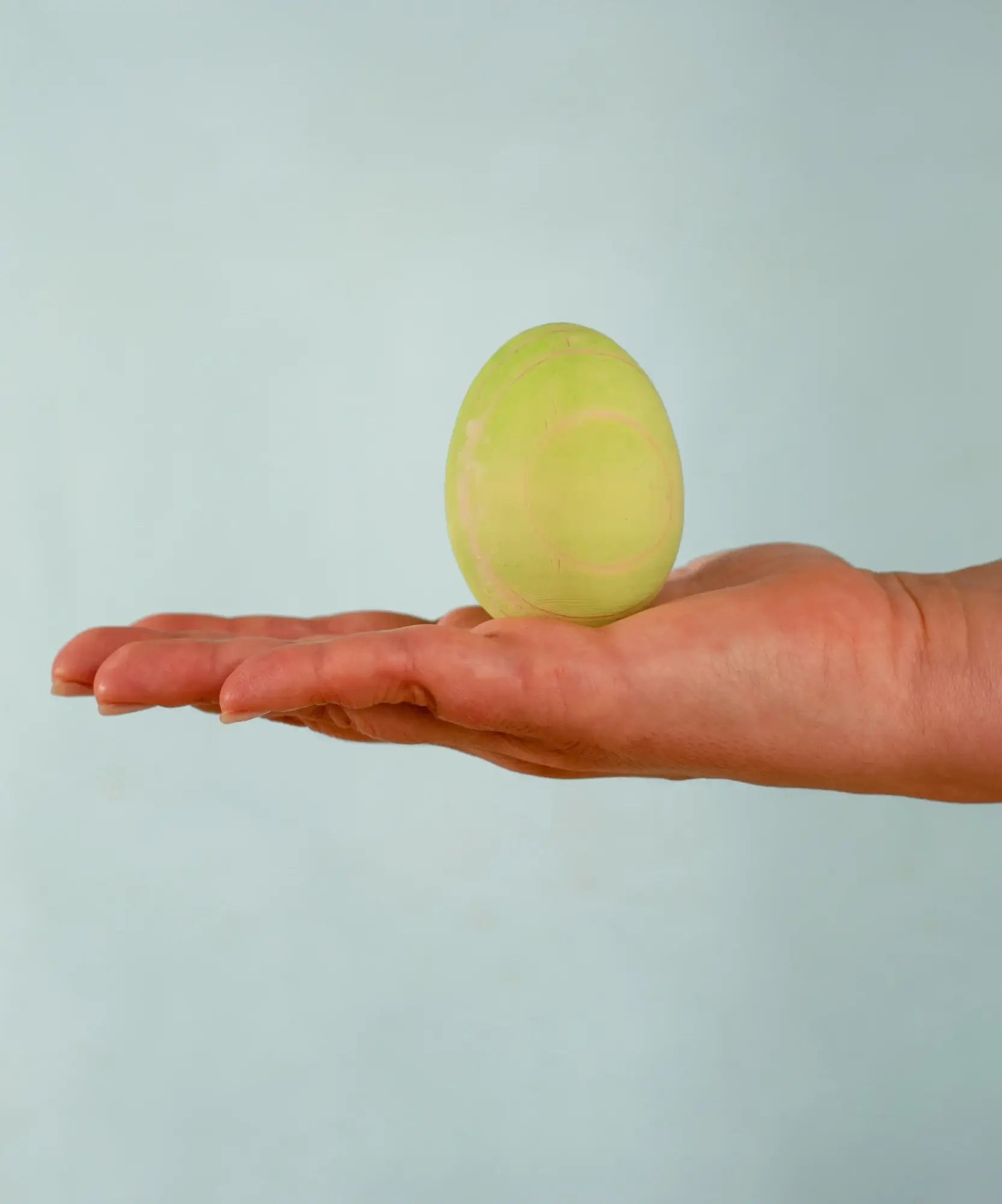 Adult hand holding the Bumbu handcrafted festive green egg decorative figure showing size