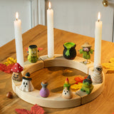 Nine Bumbu Halloween themed celebration ring figures placed on a natural wooden celebration ring with three candles lit. 
