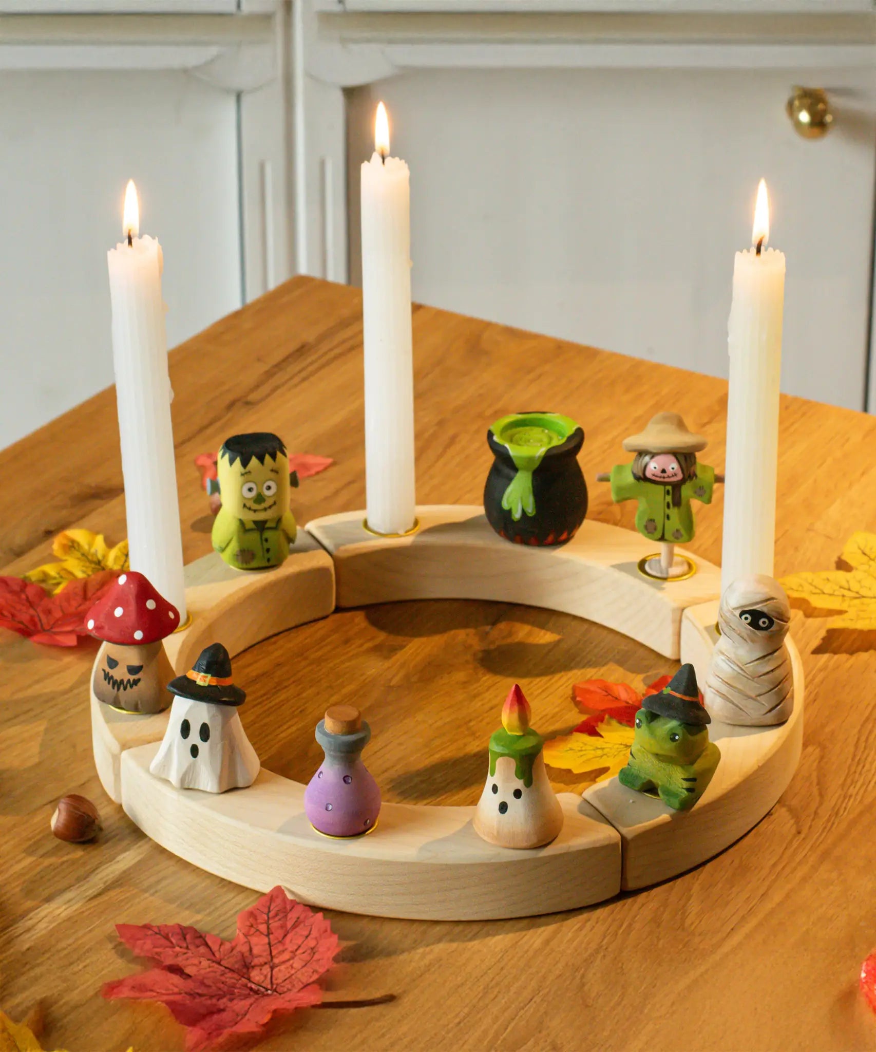 Nine Bumbu Halloween themed celebration ring figures placed on a natural wooden celebration ring with three candles lit. 