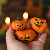 Bumbu set of 3 Halloween pumpkins held in an adult's hand to show scale. A Grimm's celebration ring with lit candles can be seen in the background. These wooden figures are part of a wide range of expertly hand crafted wooden toys here at Babipur. 